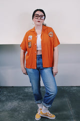 Men's vintage 1960's Joel's Striker short sleeve orange button up bowling shirt with three patches sewn on. Rayon acrylic blend material. One chest pocket and small collar.