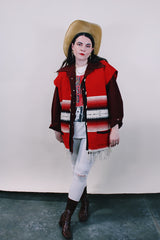 Women's or men's vintage boho western style 1970's sleeveless red wool vest with black trim, cream fringe trim on hem, and black and cream stripes.