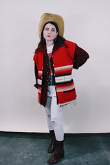 Women's or men's vintage boho western style 1970's sleeveless red wool vest with black trim, cream fringe trim on hem, and black and cream stripes.