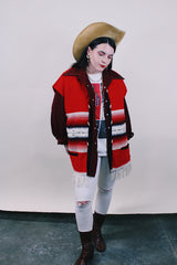 Women's or men's vintage boho western style 1970's sleeveless red wool vest with black trim, cream fringe trim on hem, and black and cream stripes.