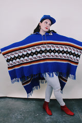 Women's or men's vintage 1970's blue acrylic material poncho with fringe trim and half zipper closure at neck. White. black, brown, and red striped print.