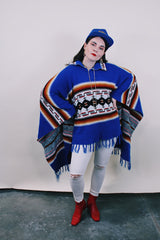 Women's or men's vintage 1970's blue acrylic material poncho with fringe trim and half zipper closure at neck. White. black, brown, and red striped print.