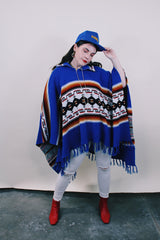 Women's or men's vintage 1970's blue acrylic material poncho with fringe trim and half zipper closure at neck. White. black, brown, and red striped print.