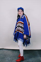 Women's or men's vintage 1970's blue acrylic material poncho with fringe trim and half zipper closure at neck. White. black, brown, and red striped print.