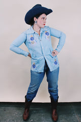 Women's or men's vintage 1970's long sleeve light wash denim shirt with popper buttons, pockets, belt loops, and floral embroidery throughout.