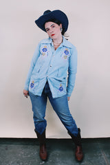 Women's or men's vintage 1970's long sleeve light wash denim shirt with popper buttons, pockets, belt loops, and floral embroidery throughout.