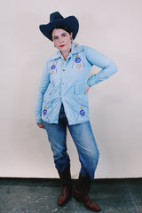 Women's or men's vintage 1970's long sleeve light wash denim shirt with popper buttons, pockets, belt loops, and floral embroidery throughout.