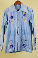 Women's or men's vintage 1970's long sleeve light wash denim shirt with popper buttons, pockets, belt loops, and floral embroidery throughout.