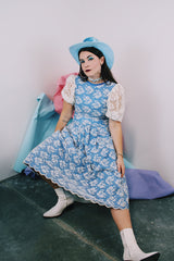 Women's vintage 1980's blue polyester dress with a white lace overlay. Has sheer puff sleeves, side zipper, low cut back, and a lace bow in the back