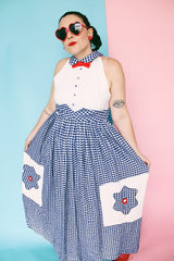 Women's vintage 1970's sleeveless halter neck maxi style halter dress in white and navy gingham print with red bowtie at neck and two front pockets on skirt with flowers.