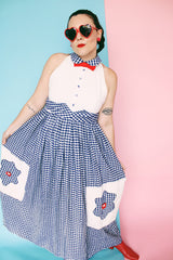 Women's vintage 1970's sleeveless halter neck maxi style halter dress in white and navy gingham print with red bowtie at neck and two front pockets on skirt with flowers.
