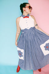 Women's vintage 1970's sleeveless halter neck maxi style halter dress in white and navy gingham print with red bowtie at neck and two front pockets on skirt with flowers.
