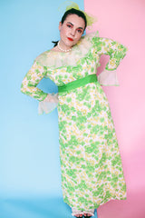 Women's vintage 1970's long sleeve maxi length floral print dress in green and white colors. Sheer white ruffle trim, ribbon belt.