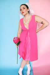 Women's vintage 1960's sleeveless mini length babydoll dress in bright pink with V shaped neckline and bow on chest.