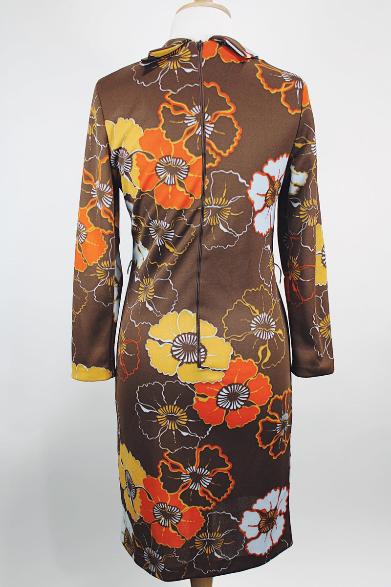 Women's vintage 1970's long sleeve knee length dress in a polyester material with a tie front neck. Brown color with all over yellow and orange flowers. 