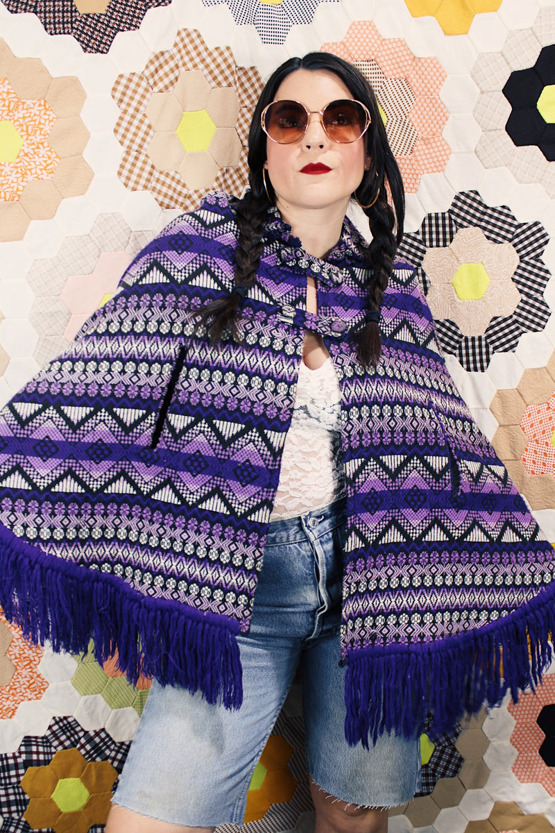 Women's vintage 1970's Made in Guatemala label purple and white printed poncho with fringe trim and two button closure across chest.