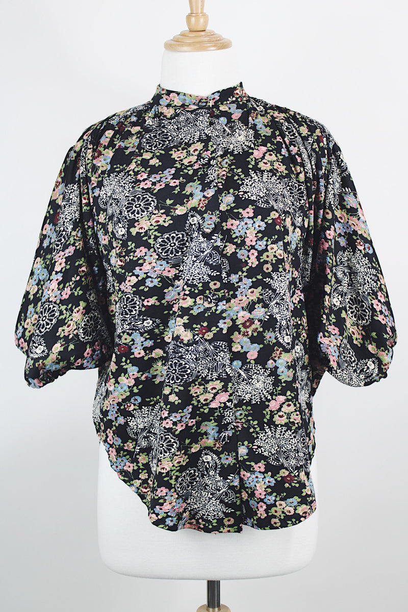 Women's vintage 1970's lightweight polyester material black blouse with all over multicolored ditsy floral print. Buttons up the front and has big wing sleeves.