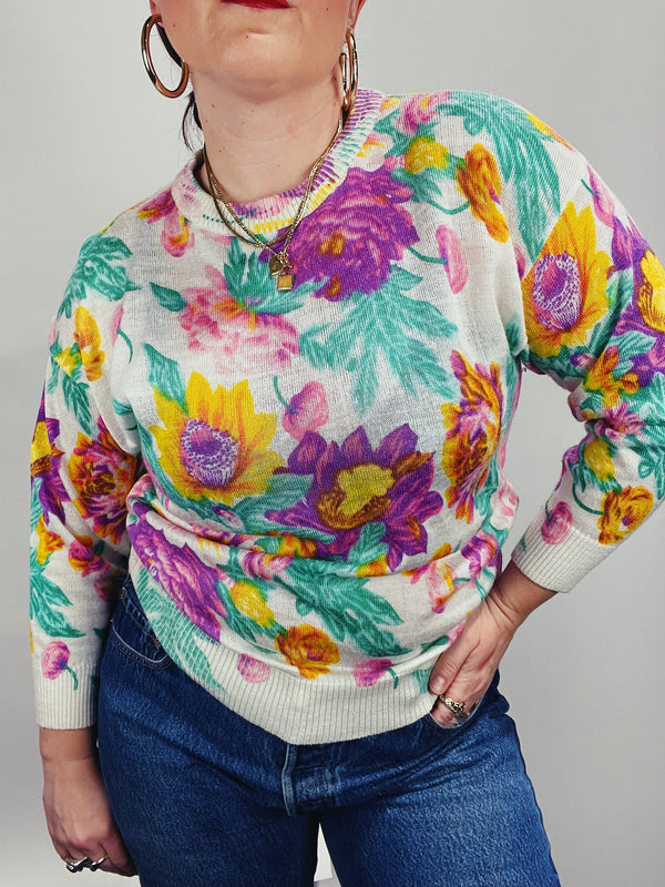Women's vintage 1980's Sweater Teas label long sleeve white pullover acrylic sweater with all over large floral print in purple, yellow, and green. 
