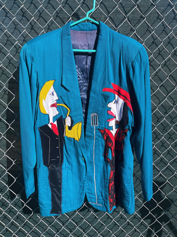 Women's vintage 1980's made in usa long sleeve blue blazer with one button closure and fully lined with large patches of people on front and back. 