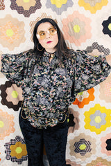 Women's vintage 1970's lightweight polyester material black blouse with all over multicolored ditsy floral print. Buttons up the front and has big wing sleeves.
