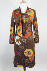 Women's vintage 1970's long sleeve knee length dress in a polyester material with a tie front neck. Brown color with all over yellow and orange flowers. 