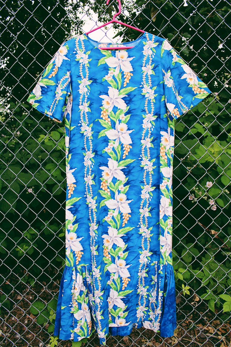 Women's vintage 1970's short sleeve Hawaiian print dress in blue with white flowers. Ruffle hem and maxi length.