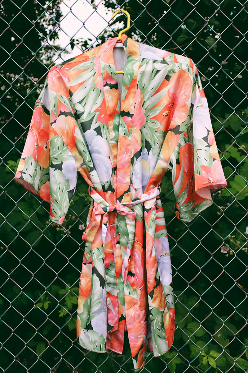 Women's vintage 1990's Val Mode Lingerie, Made in USA label short sleeve short length loungewear robe in an all over tropical floral print in orange and green with a matching tie belt. 