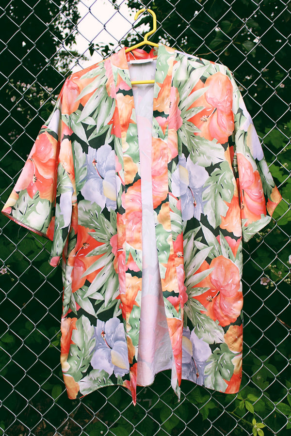 Women's vintage 1990's Val Mode Lingerie, Made in USA label short sleeve short length loungewear robe in an all over tropical floral print in orange and green with a matching tie belt. 