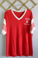 Women's or men's vintage 1980's short sleeve red tee with white trim around v shaped neckline. White sleeves have red stripes. White graphic on left chest.