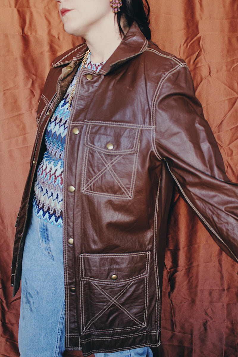 Women's or men 's vintage 1970's Montgomery Ward label long sleeve chocolate brown colored leather jacket with contrast stitching and popper buttons.