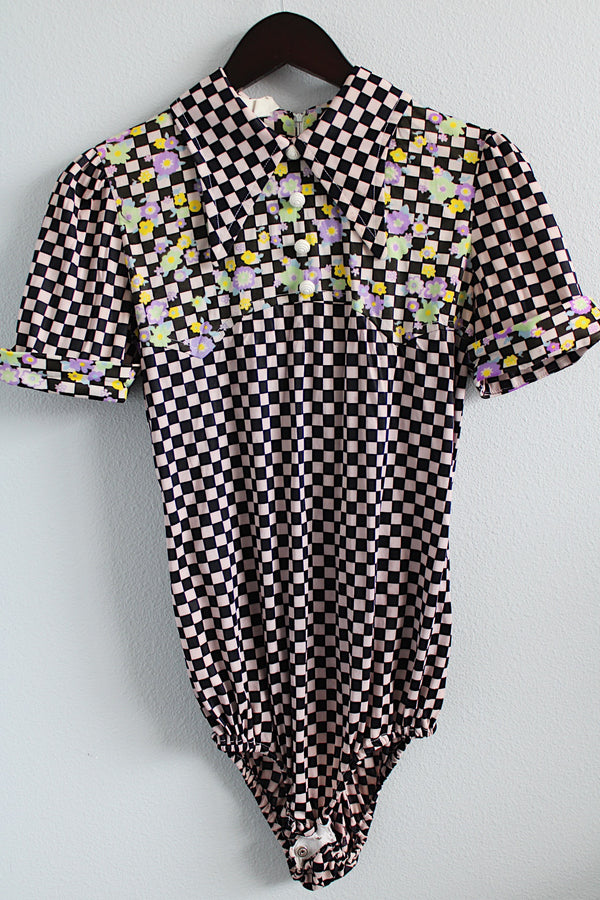 Women's vintage 1970's short sleeve puff sleeve bodysuit with collar in a black and purple checkered print and florals. 