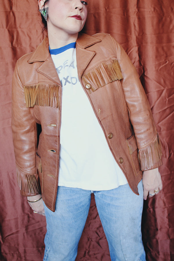 Women's vintage 1950's Custom Made by Milco-West, Portland, Oregon label long sleeve button up tan camel colored leather jacket with fringe trim. Western style with four pockets.