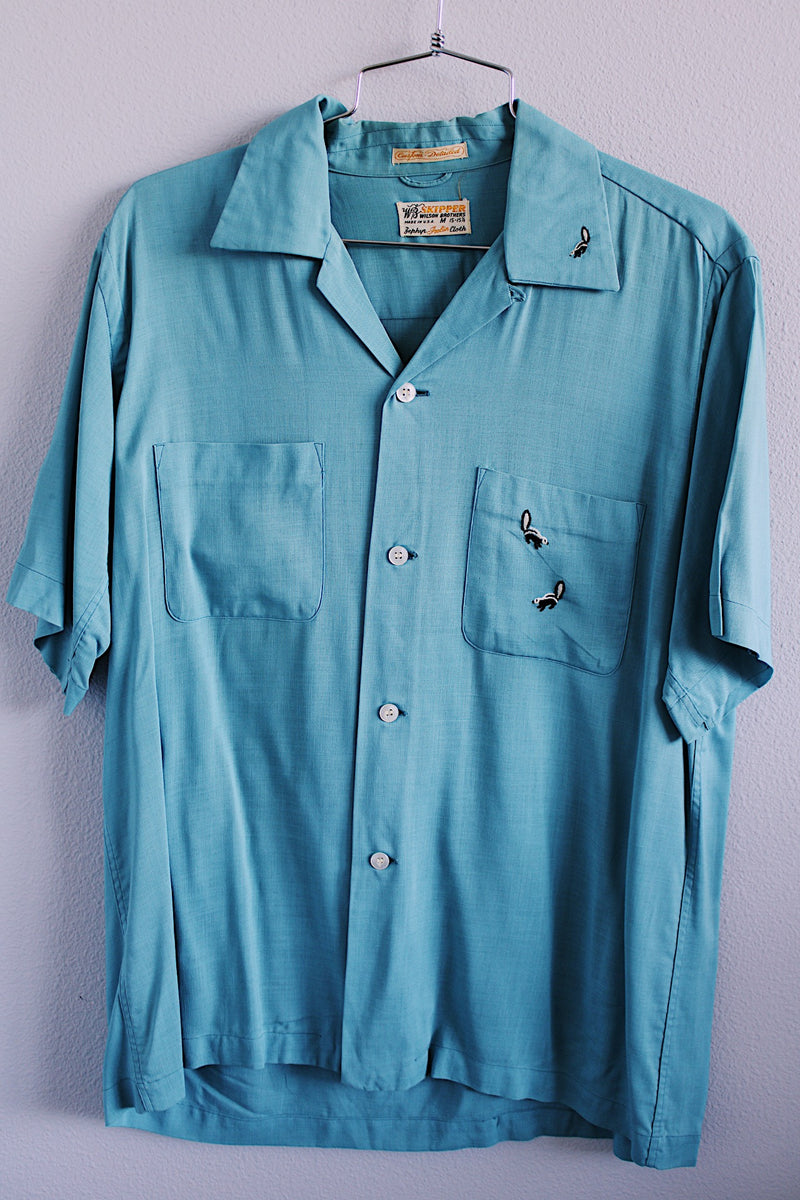 Men's vintage 1950's Skipper, Wilson Brothers, Made in USA, Custom Detailed label short sleeve blue button up shirt in cotton material with small embroidered skunks. 