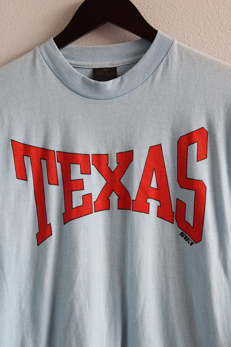 Men's or women's vintage 1980's Touch of Gold, Made in USA label long sleeve light blue t-shirt with red text on front that reads Texas in a polyester and cotton material.