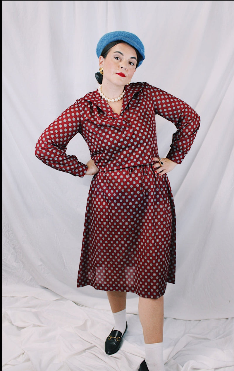 Women's vintage 1970's long sleeve midi length lightweight polyester dress with v shaped neckline and collar. Cinched at waist with tie. Maroon with all over blue and tan print.