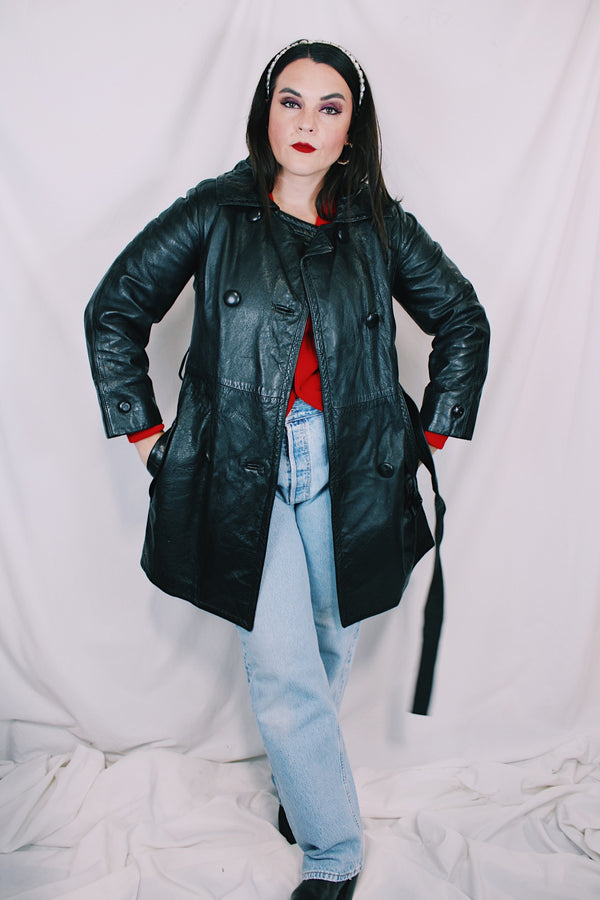 Women's vintage 1970's long sleeve double breasted long length black leather jacket with fabric buttons and side pockets. Matching belt. 