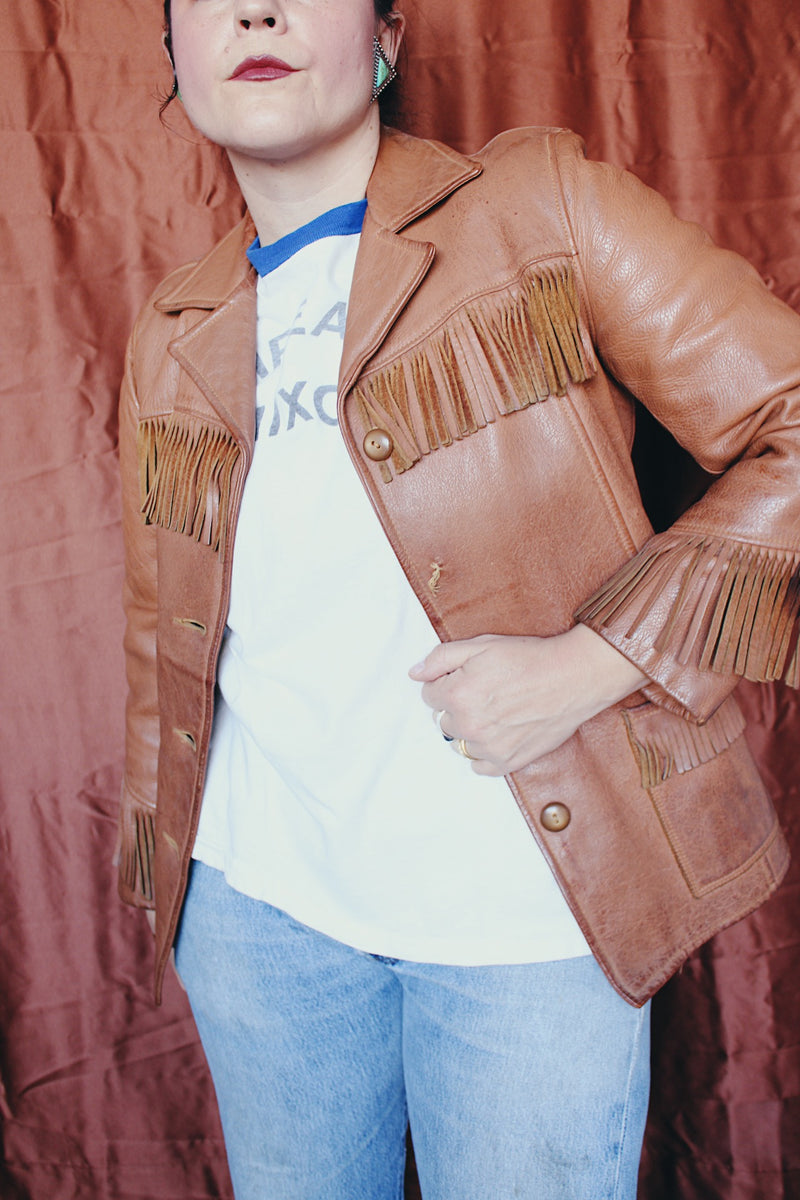 Women's vintage 1950's Custom Made by Milco-West, Portland, Oregon label long sleeve button up tan camel colored leather jacket with fringe trim. Western style with four pockets.