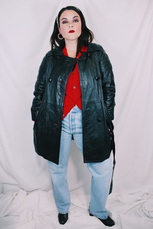 Women's vintage 1970's long sleeve double breasted long length black leather jacket with fabric buttons and side pockets. Matching belt. 