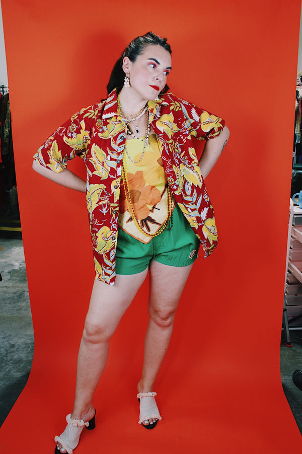 Women's or men's vintage 1970's Sundek, Made in USA label short sleeve button up shirt with dagger collar in cotton material with all over Hawaiian print in red, yellow, and green colors.