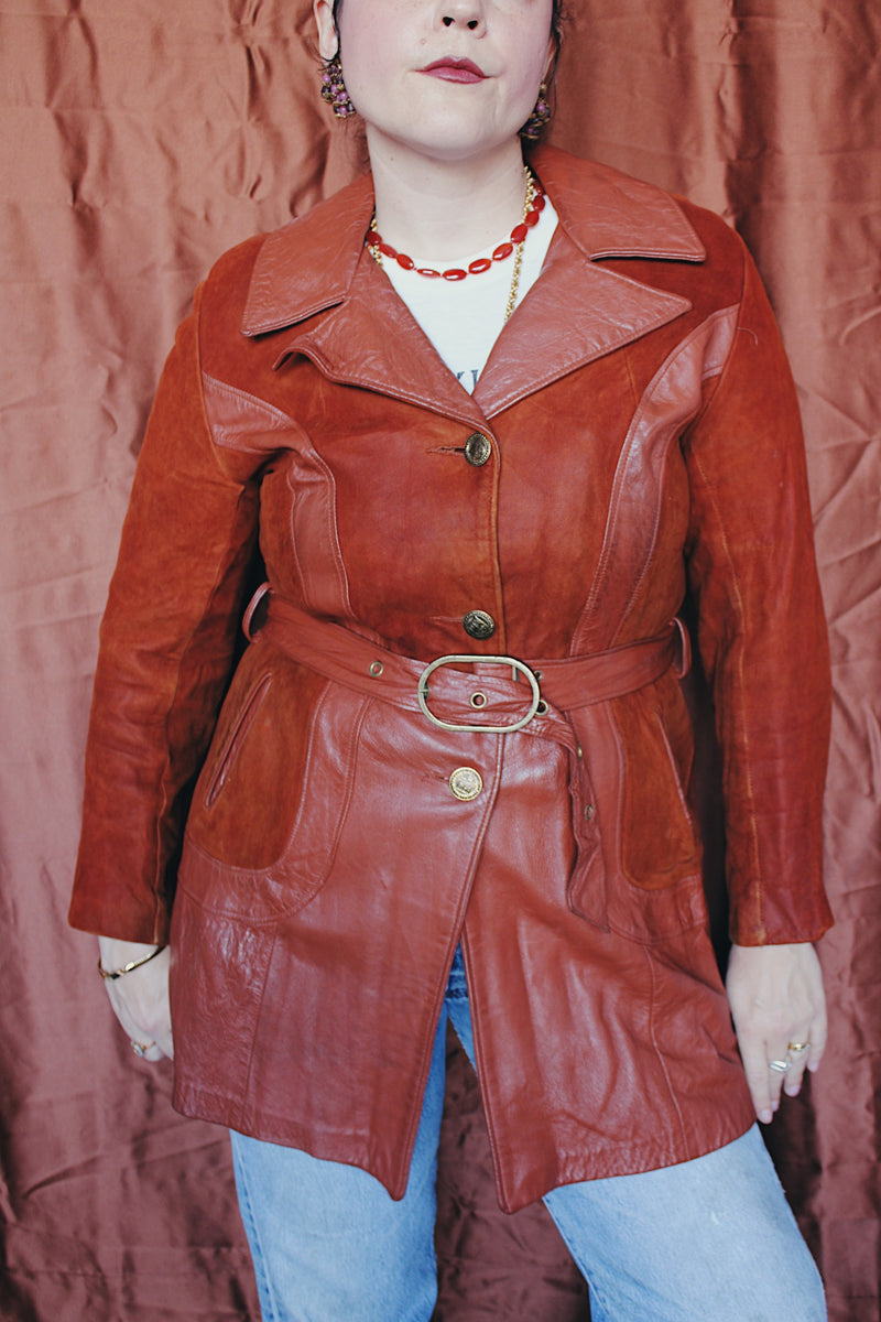 Women's vintage 1970's long sleeve button up burnt orange suede and leather jacket. Long length with matching belt.