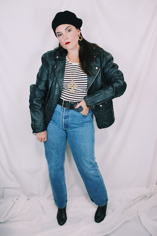 Men's or women's vintage 1980's long sleeve black leather moto jacket with all over silver hardware. Snap buttons, pockets with zippers, and zipper closure. 
