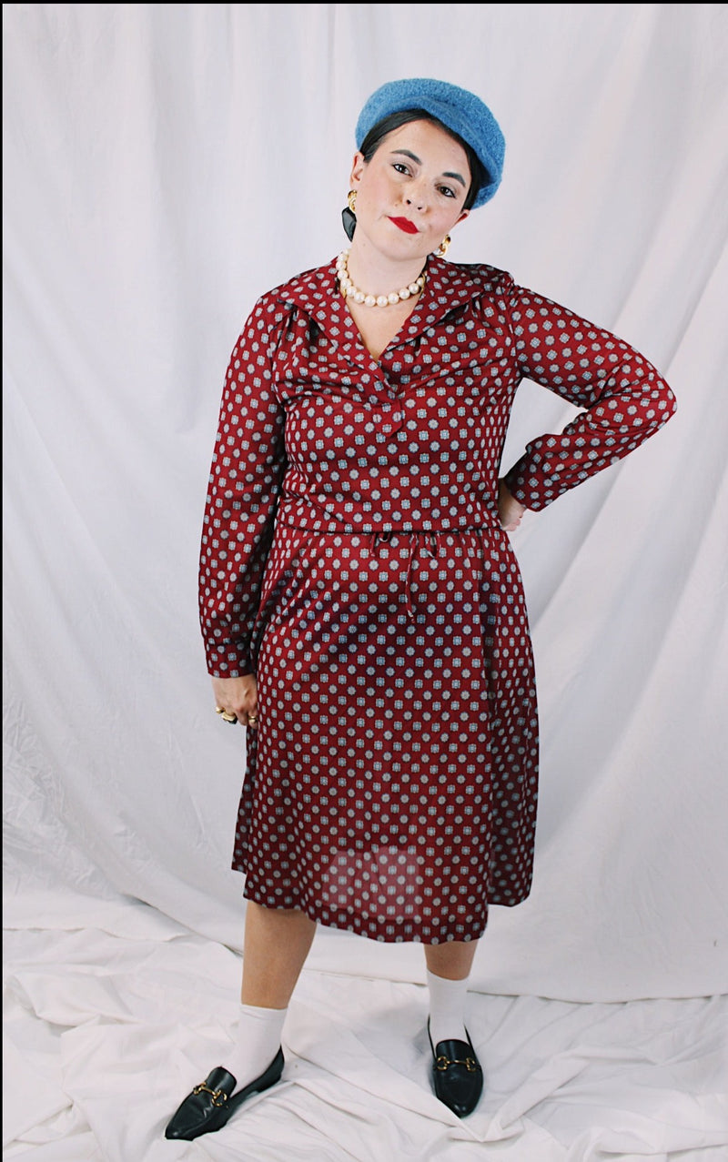 Women's vintage 1970's long sleeve midi length lightweight polyester dress with v shaped neckline and collar. Cinched at waist with tie. Maroon with all over blue and tan print.