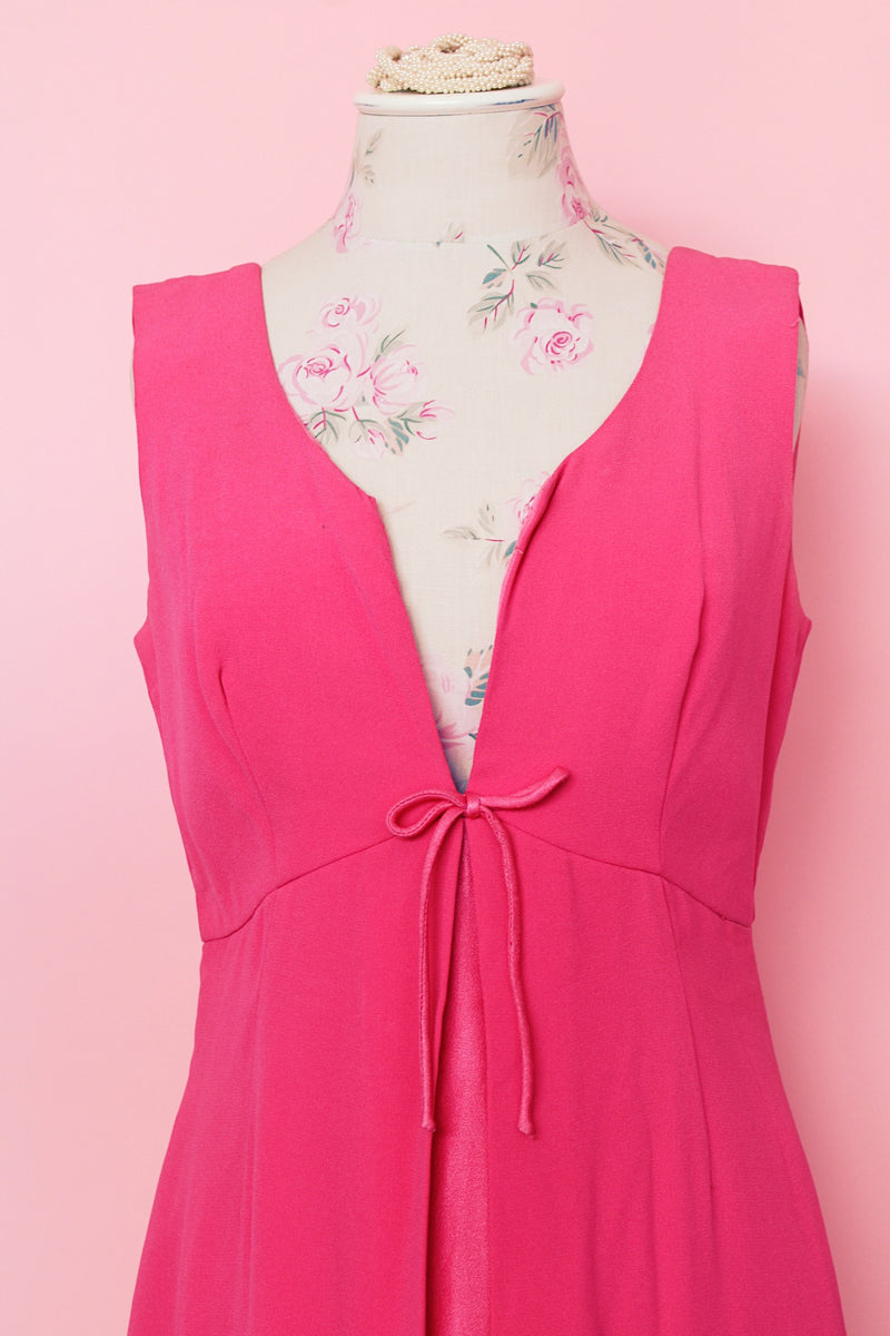 Women's vintage 1960's sleeveless mini length babydoll dress in bright pink with V shaped neckline and bow on chest.