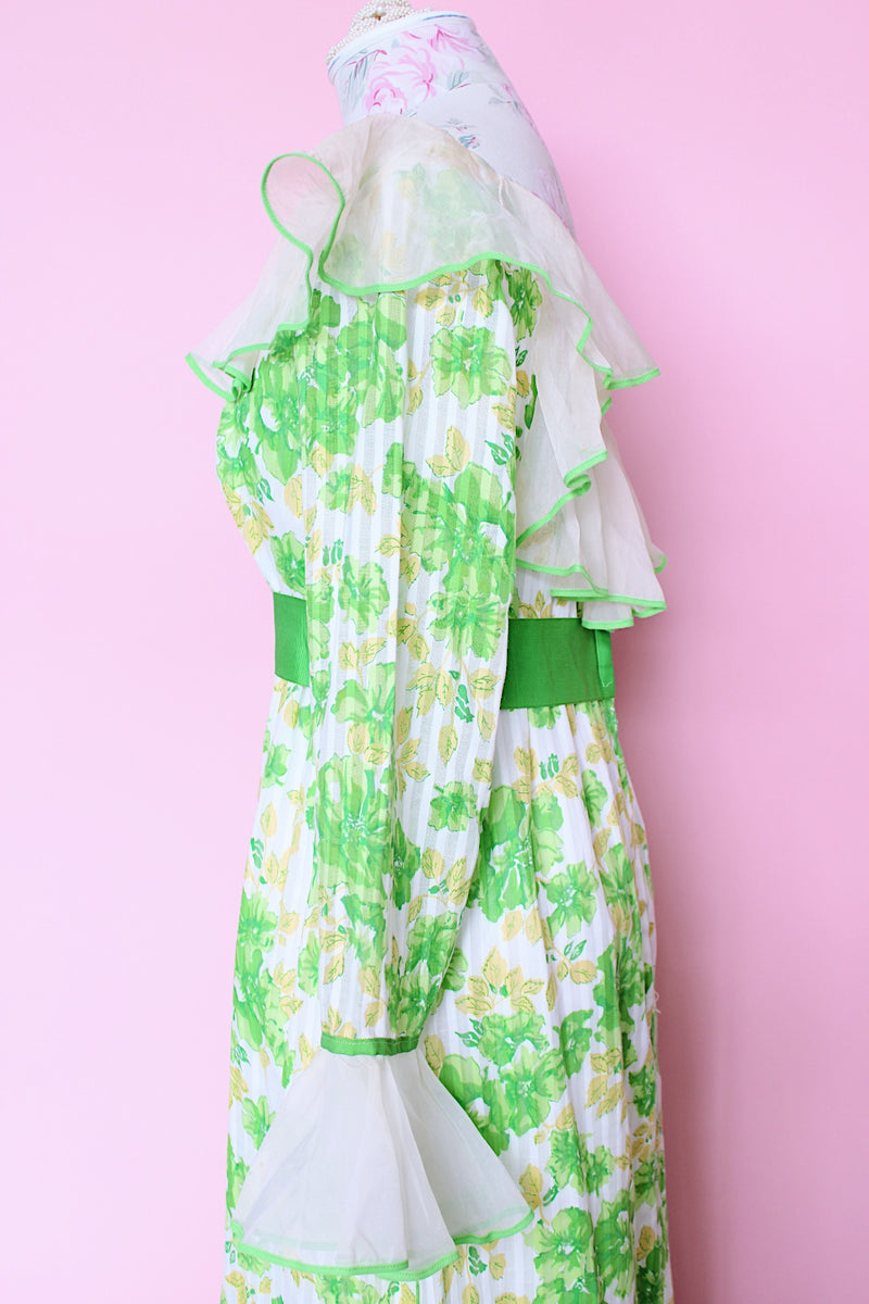 Women's vintage 1970's long sleeve maxi length floral print dress in green and white colors. Sheer white ruffle trim, ribbon belt.