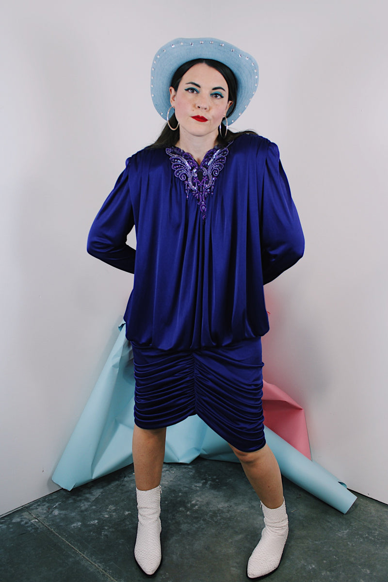 Women's vintage 1980's long sleeve knee length drapey purple slinky polyester dress with beaded trim neckline.
