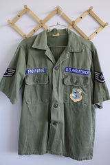 Men's vintage 1960's Guaranteed Trooper Fatigues label short sleeve army green button up shirt or jacket with US Air Force patches all over. 