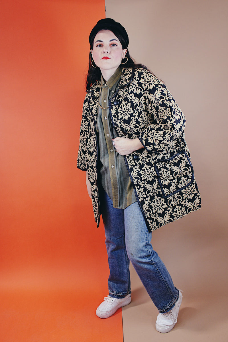 Women's vintage 1960's black and tan tapestry printed button up coat with black leather trim, two front pockets, and a rounded peter pan collar