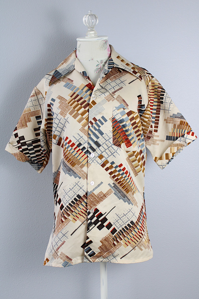 Men's vintage 1970's Jandy Place, Bardon Inc. label short sleeve button up shirt with a pointy collar in a silk like polyester material cream colored with all over brown and blue abstract print. 