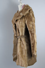 Women's vintage 1960's long sleeve knee length faux fur tan coat with leather trim. Has a matching leather belt, gold twist buttons, and pockets