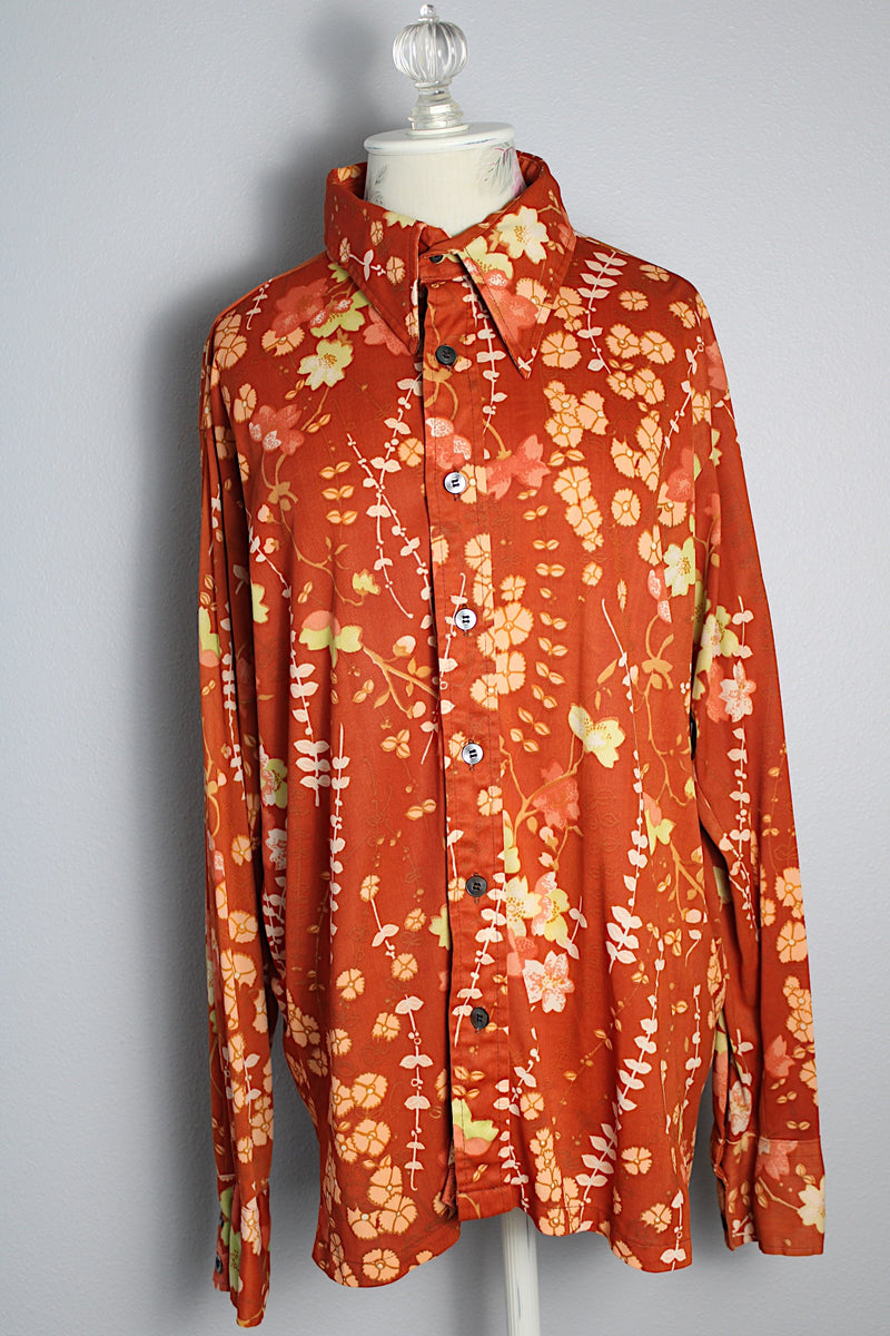 Women's or men's vintage 1970's Custom Tailored label long sleeve button up shirt with pointy collar in a lightweight Polyester material. Burnt orange with all over green and peach colored floral print. 